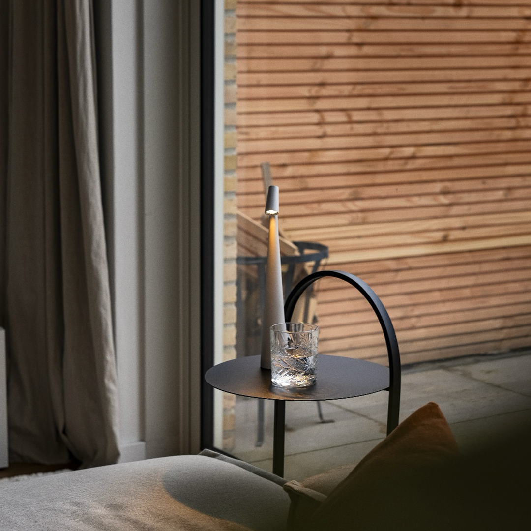 LED-Tischlampe auf runder Glasplatte neben Fenster mit Jalousie