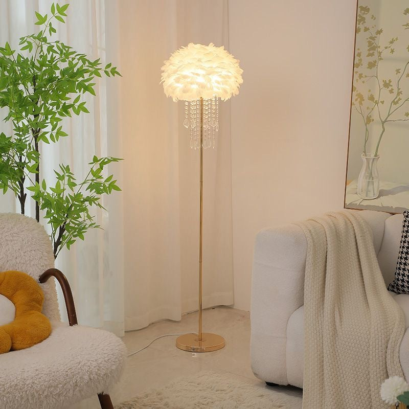 Feder-Stehlampe mit goldenem Fuß in hellem Wohnzimmer neben einem Rattanstuhl