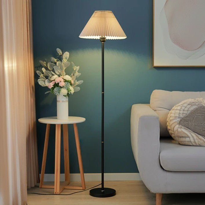 Stehlampe mit plissiertem Schirm neben Sofa und Blumenarrangement auf Beistelltisch