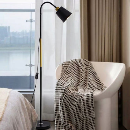 Schwarze Stehlampe mit gebogenem Arm und Holzdetail neben Sessel am Fenster

