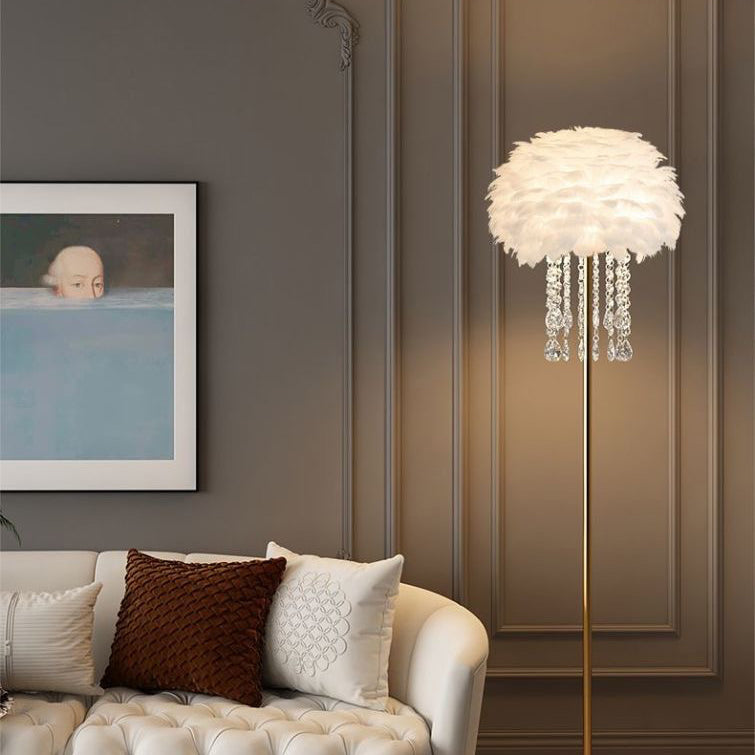 Kuschelige Feder-Stehlampe mit goldfarbenem Standfuß vor Wand mit Bilderrahmen