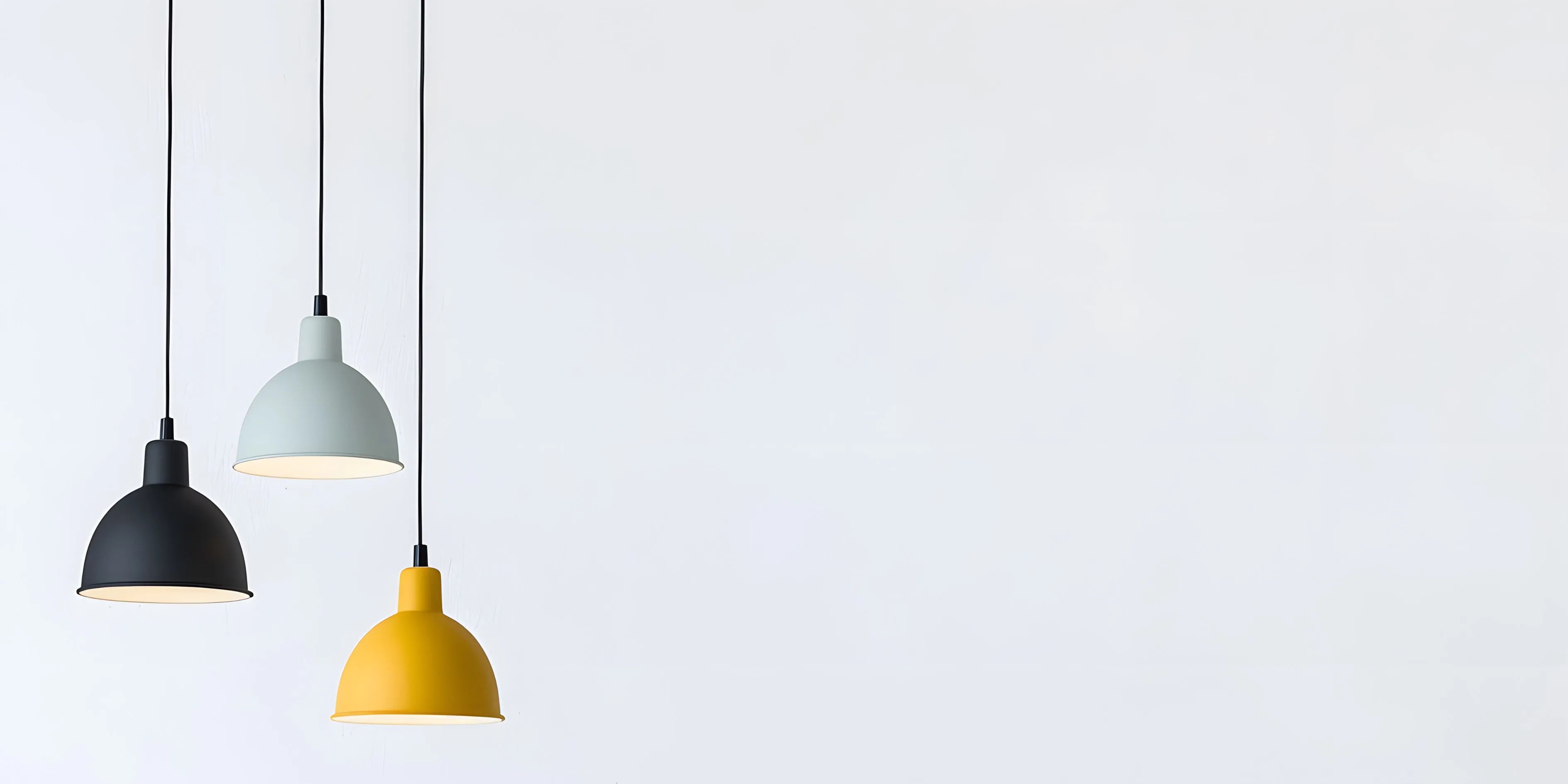 Drei moderne Pendelleuchten in Schwarz, Hellgrau und Gelb vor hellem Hintergrund